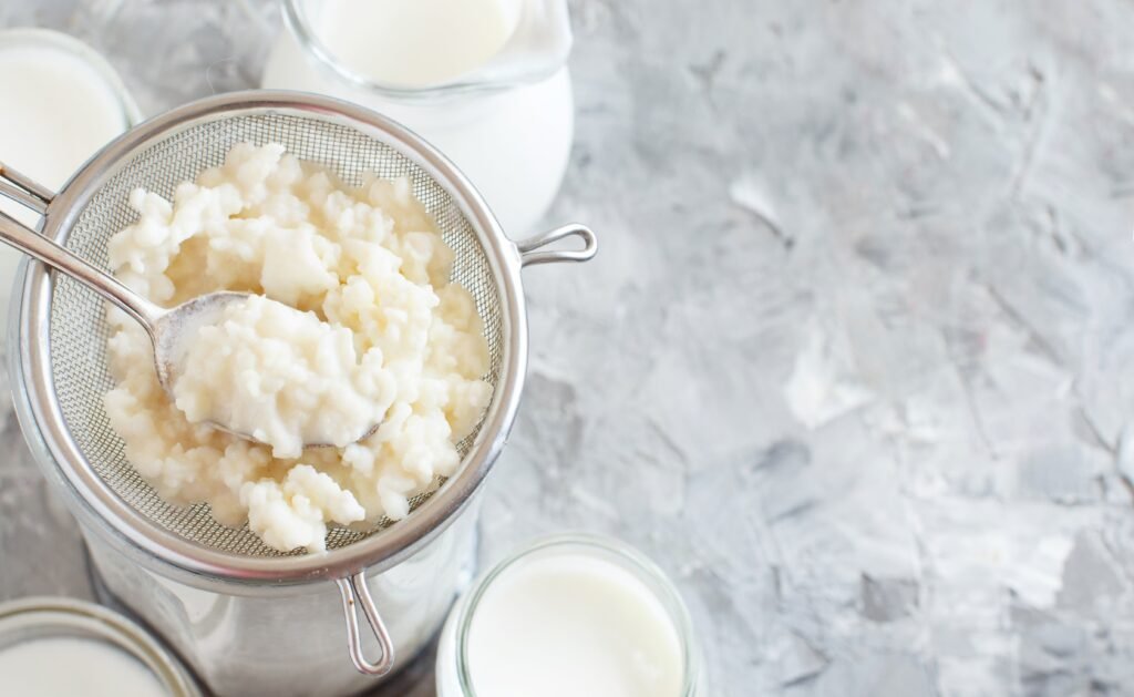 kefir grains being strained from the kefir mixture on a bright colored countertop with other kefir batches in the background